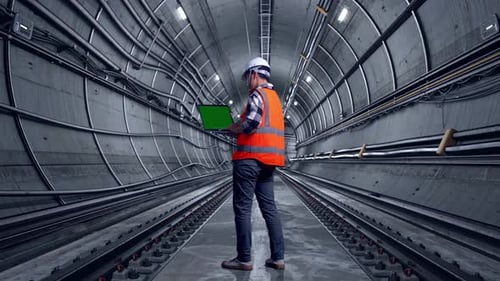 Full Body Back View Of Asian Male Engineer Working On A Green Screen Laptop In Subway Tunnel