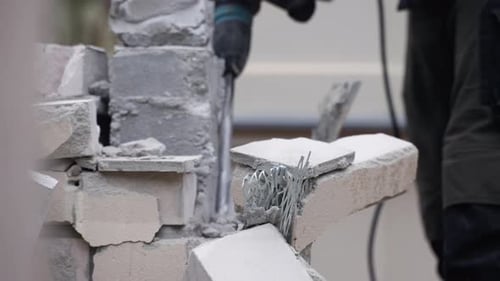 Hombre irreconocible que usa un martillo neumático para demoler una pared de ladrillos: cámara lenta de primer plano