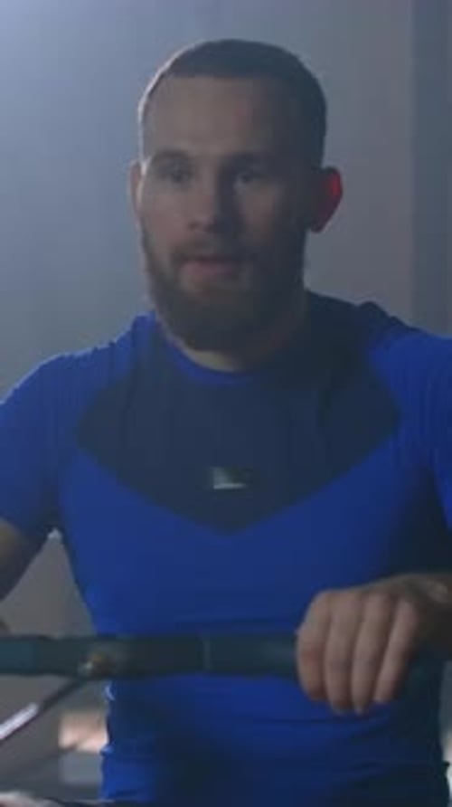 Focused Athletic Man Training on Indoor Rowing Machine in Dimly Lit Gym Demonstrating Intense Full