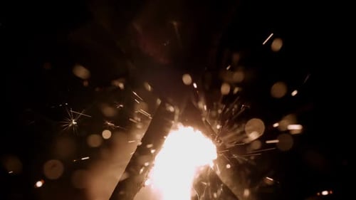 Close-up Of Two Burning Sparklers Against A Dark Background