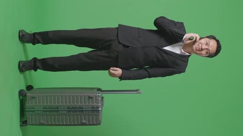 Full Body Of Asian Businessman With Luggage Talking On Smartphone While Standing In The Green Screen