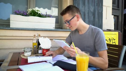 Teenage boy with tablet studies homework at cafe table in the city