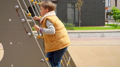 Little boy climbing up the net at public playground