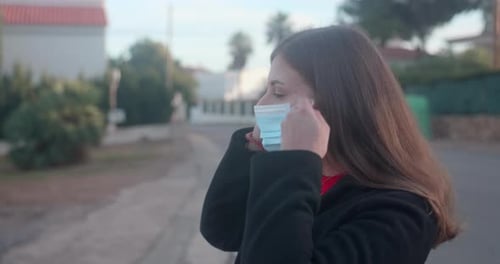 Woman putting on a surgical mask in the street. Coronavirus (Covid-19) pandemic.