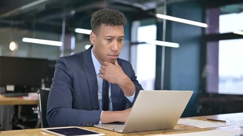 Young Adult Thinking at Desk in Modern Office