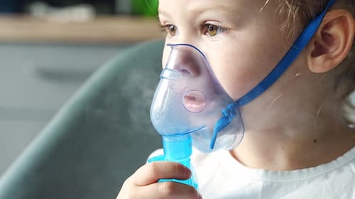 Une jolie petite fille est assise et tient un masque de nébulisation appuyé contre le traitement des voies respiratoires du visage