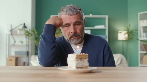Man Sits Alone at Birthday Cake Blowing Candle