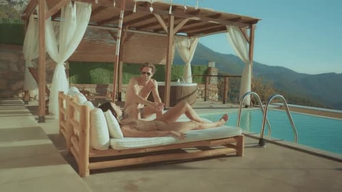 Couple relaxing on a daybed by a pool with a scenic mountain view