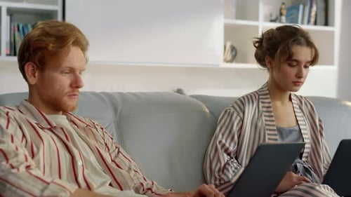 Couple working on laptops together at home on couch