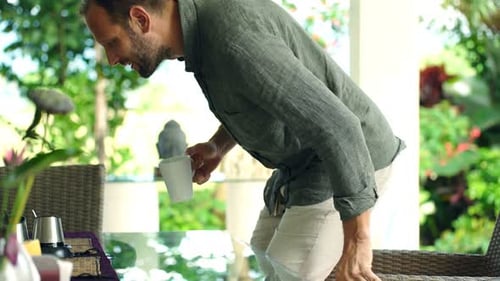 Happy young man enjoys beverage and garden view on relaxing sunny day
