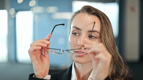 Focused Businesswoman Puts On Eyeglasses in Office