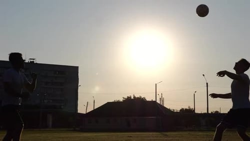 Silhouette of Professional Footballers Kicking Soccer Ball with Their Heads on Stadium at Sunset Two