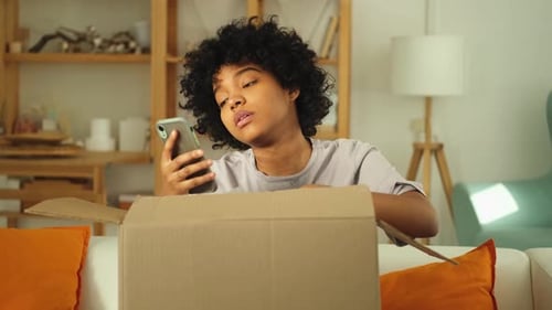 Young Woman Opens Box While Using Phone