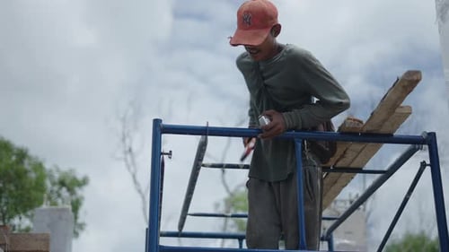Laborer At Work Going Down On A Scaffolding Holding Level Bar And Meter Tape At Building Site