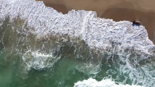 Vista aérea de las olas del océano que bañan una apartada playa costera de arena