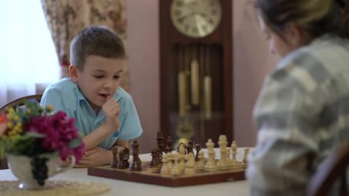 Concentrating Child Plays Chess at Home with Woman