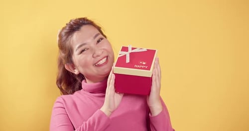 Close up woman holds a red gift box with good emotions smiling and lovely on bright yellow backgroun