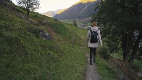 Young Woman Traveler Walks on the Slopes of the Mountains Near a Mountain Town Along Majestic