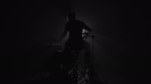 Silhouette eines männlichen Schlagzeugers, der im Dunkeln Schlagzeug spielt