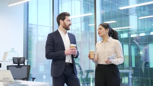 Two colleagues engaged in friendly conversation with coffee in modern office setting. Co-workers,