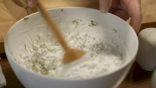 Mixing fresh herb yogurt sauce with a wooden spoon in a white bowl