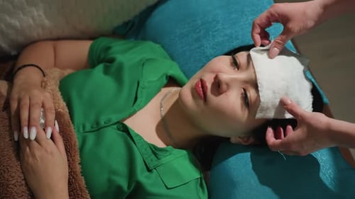 Asian Woman Resting with Cool Compress Over Eyes Therapist Hands Adjusting Cotton and Cloth Teal