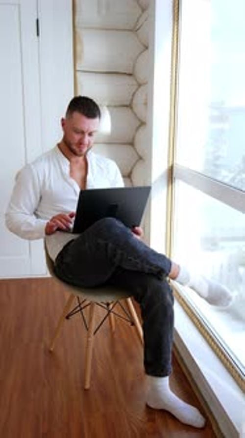 Man Working on Laptop by Window at Home