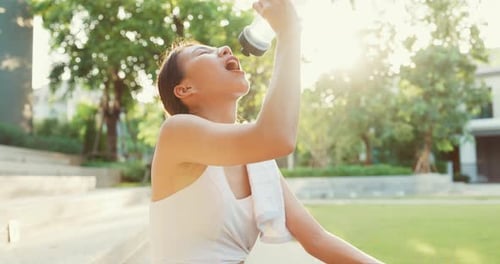 lady exercises drinking water because feel tired after running in urban park.