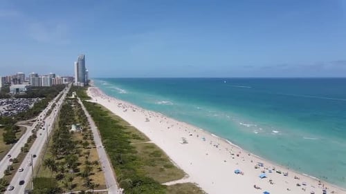 A stunning aerial view of a wide, sandy beach lined with turquoise waters, dotted with beachgoers an