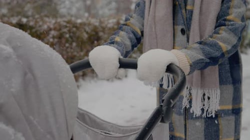 Young mother enjoys snowy winter walk with baby stroller in park