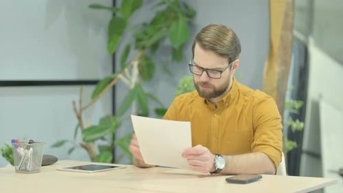Thoughtful Bearded Man Reads Paper at Desk