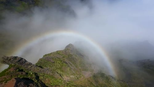 Rainbow over mountain ridge with clouds and sunlight. Aerial view from drone flying toward colorful