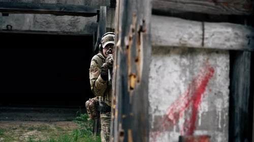 Adult Aims Rifle in Urban, Camouflage Setting