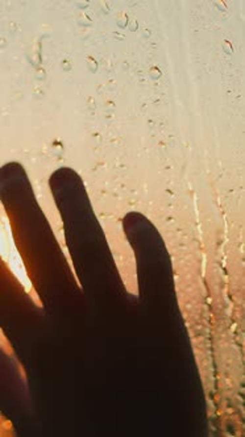 Silhouette of Hand Reaching to Red Sun Through Wet Window