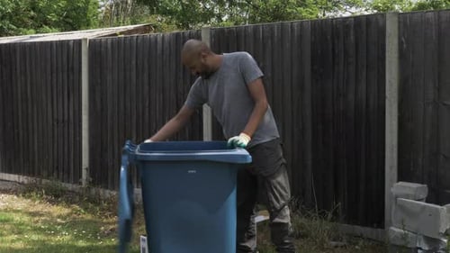 Adult UK Asian Male Sorting Cardboard Beside Blue Recycling Bin In Garden. Locked Off