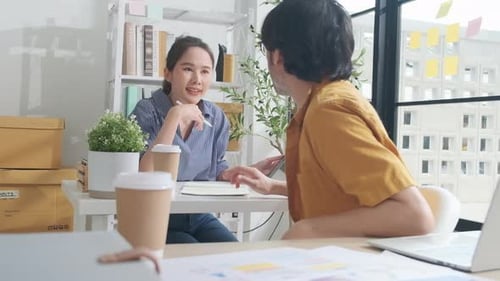 Two young Asian startup partners are working in a casual small business office.