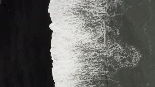 Top down aerial view of foamy waves splashing on Reynisfjara, black sand beach in Iceland