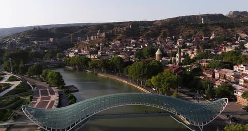 Drone Ascends Above Tbilisi Bridge of Peace on Summer Day in Georgia.