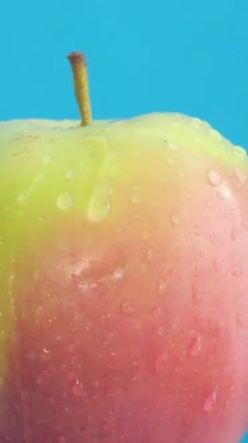 Fresh Red Green Apple on Blue Background Water Drops A Rotating Apple Closeup Vertical Video