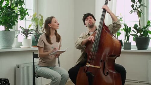 Man Plays Contrabass for Woman with Notepad