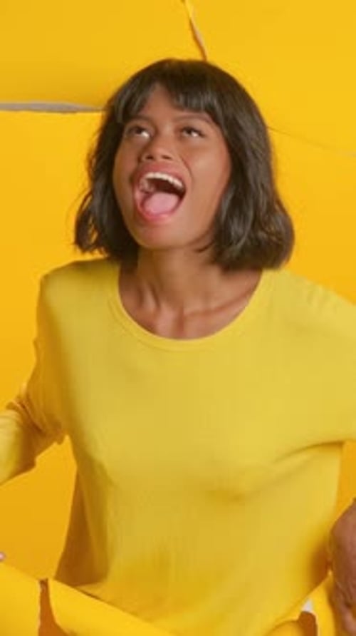 Excited Woman Breaking Through a Yellow Background