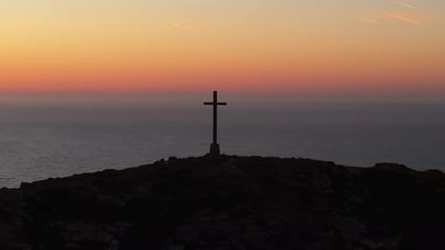 Silhouetted Cross on Hilltop at Dawn Overlooking Calm Sea
