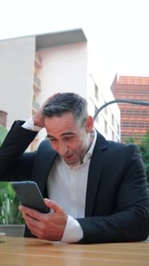 Successful Mature Businessman Expressing Joy While Using Smartphone and Laptop for Work Showing
