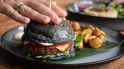 Menschliche Hand presst herzhaften schwarzen Burger mit Spieß in der Mitte