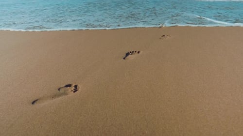 Slow-motion shot of a sea wave washing off all the footprints except for one. Summer days.