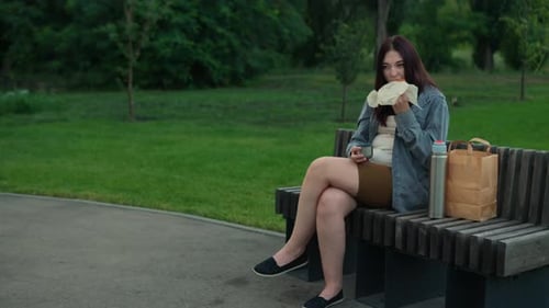 Young Woman Eating Sandwich on Park Bench