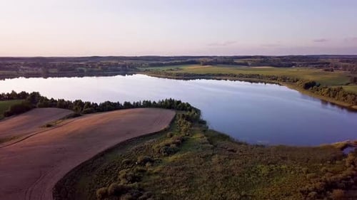 Aerial Shot of a Small, Peaceful Lake Surrounded by Trees and Farms at Sunset.