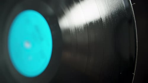 Vinyl music record with a blue label rotating on a black background, light reflection on the surface