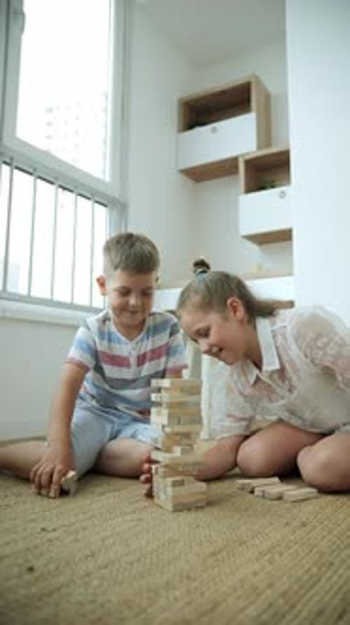 European School Boy and Girl Playing Jenga Tower in Light Room with Window