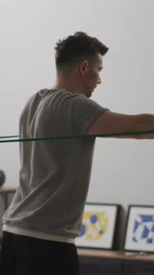 Man Performing Resistance Band Shoulder Workout at Home Focusing on Strength Training Muscle Toning